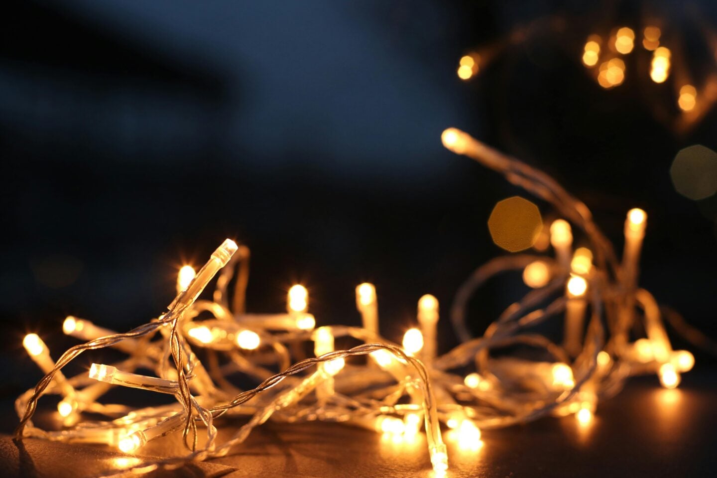 Warm yellow LED string lights tangled on a dark surface, softly glowing against a blurred, dark background.