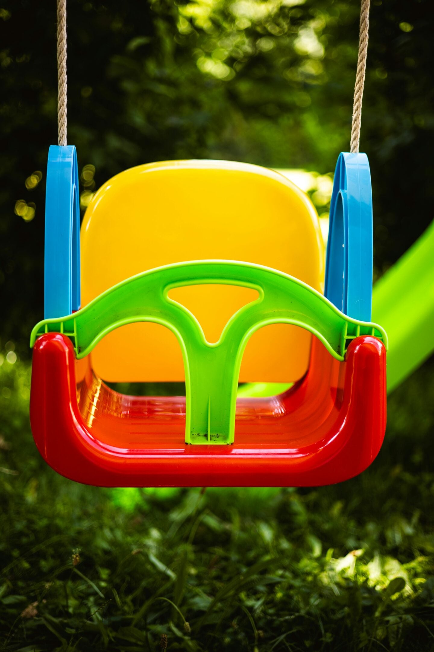 Colorful plastic swing seat attached with ropes, part of a swing set for kids in a garden, featuring a secure toddler seat design for outdoor play.