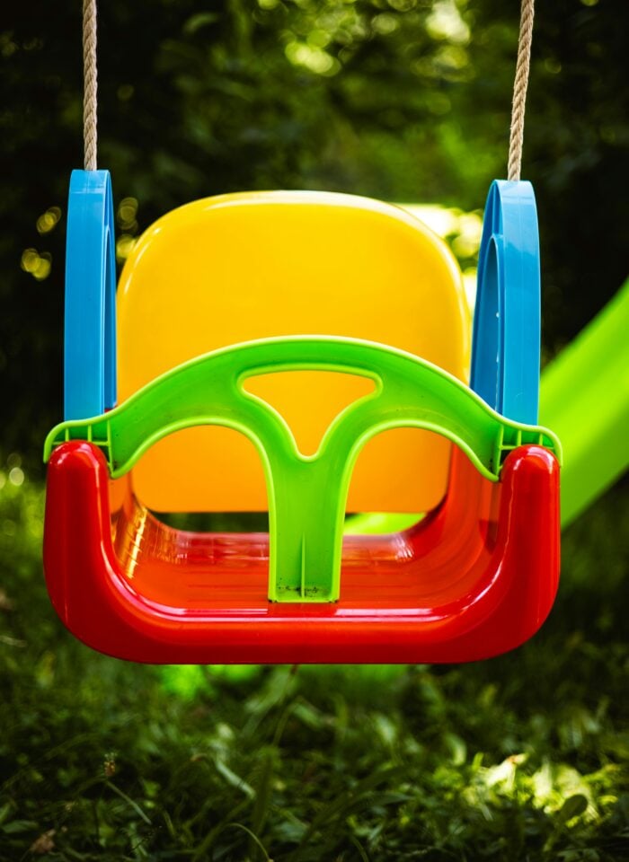 Colorful plastic swing seat attached with ropes, part of a swing set for kids in a garden, featuring a secure toddler seat design for outdoor play.