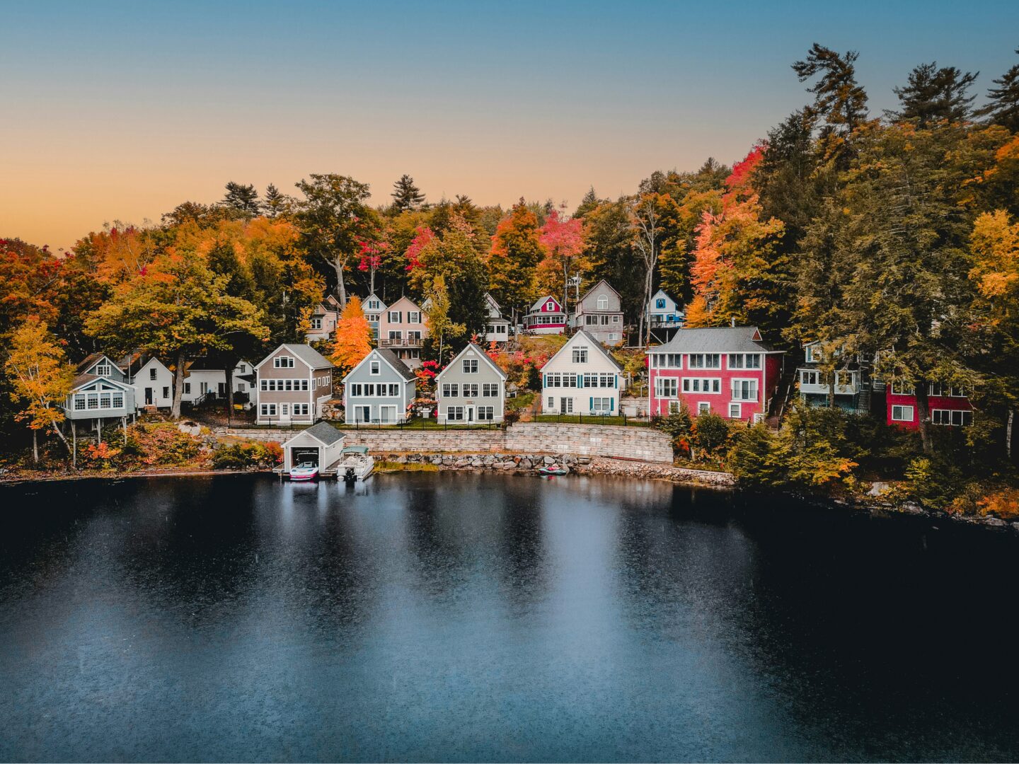 Aerial view of lakeside homes on Lake Winnipesaukee, New Hampshire, surrounded by vibrant fall foliage during peak autumn season.