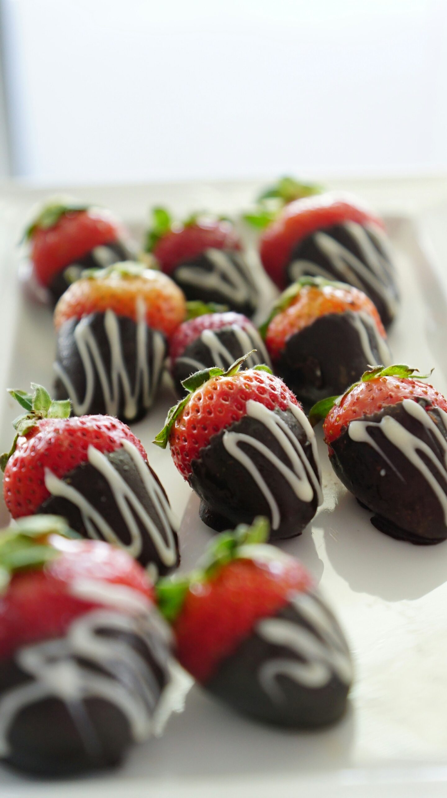 Fresh strawberries dipped in dark chocolate and drizzled with white chocolate, arranged on a white tray.