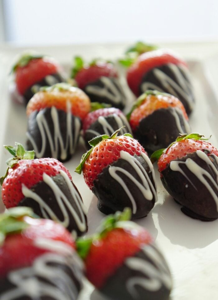 Fresh strawberries dipped in dark chocolate and drizzled with white chocolate, arranged on a white tray.