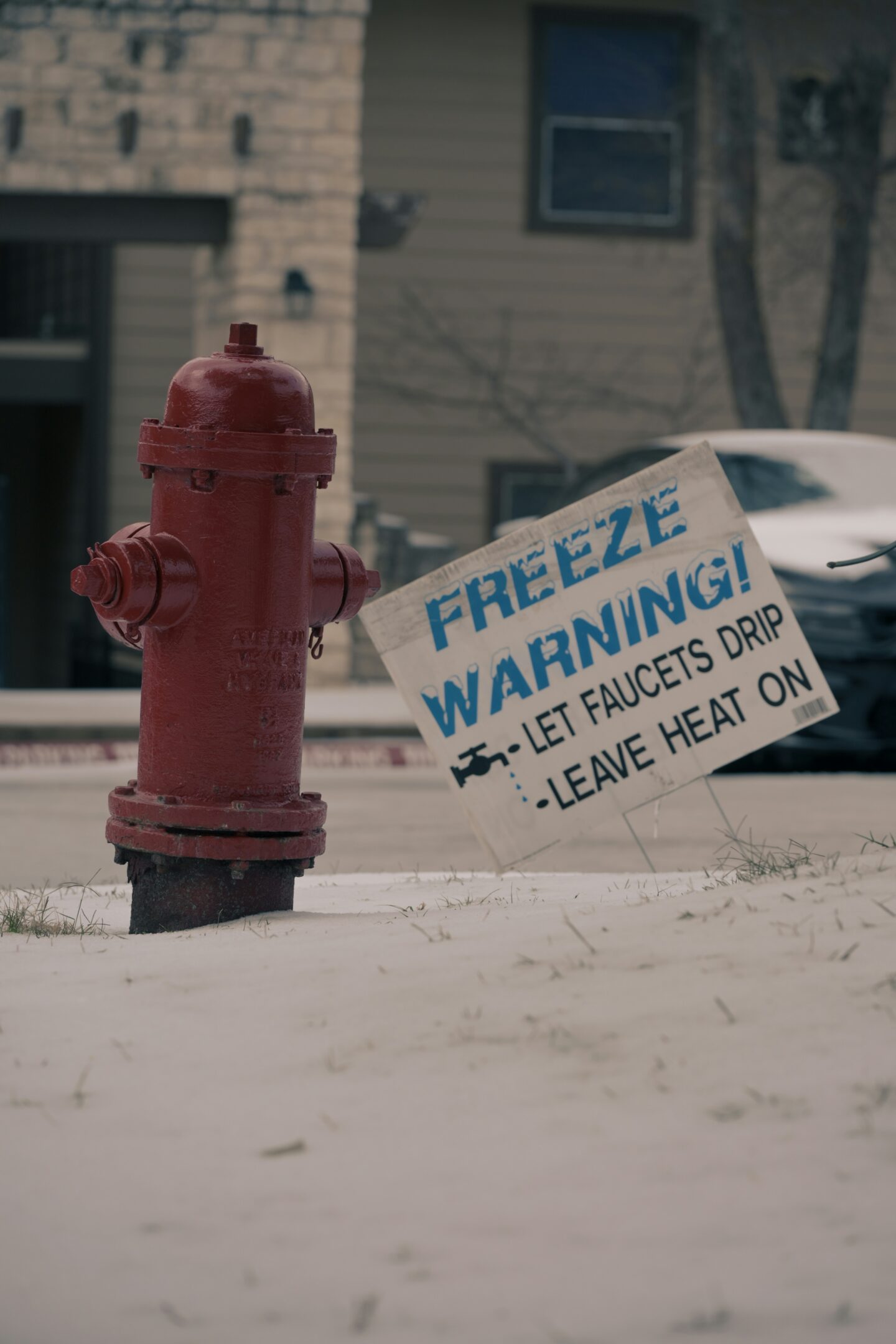 Red fire hydrant standing in snow with a freeze warning sign advising homeowners to let faucets drip and leave heat on during cold weather.