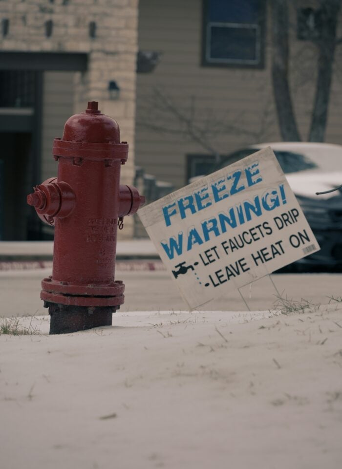 Red fire hydrant standing in snow with a freeze warning sign advising homeowners to let faucets drip and leave heat on during cold weather.