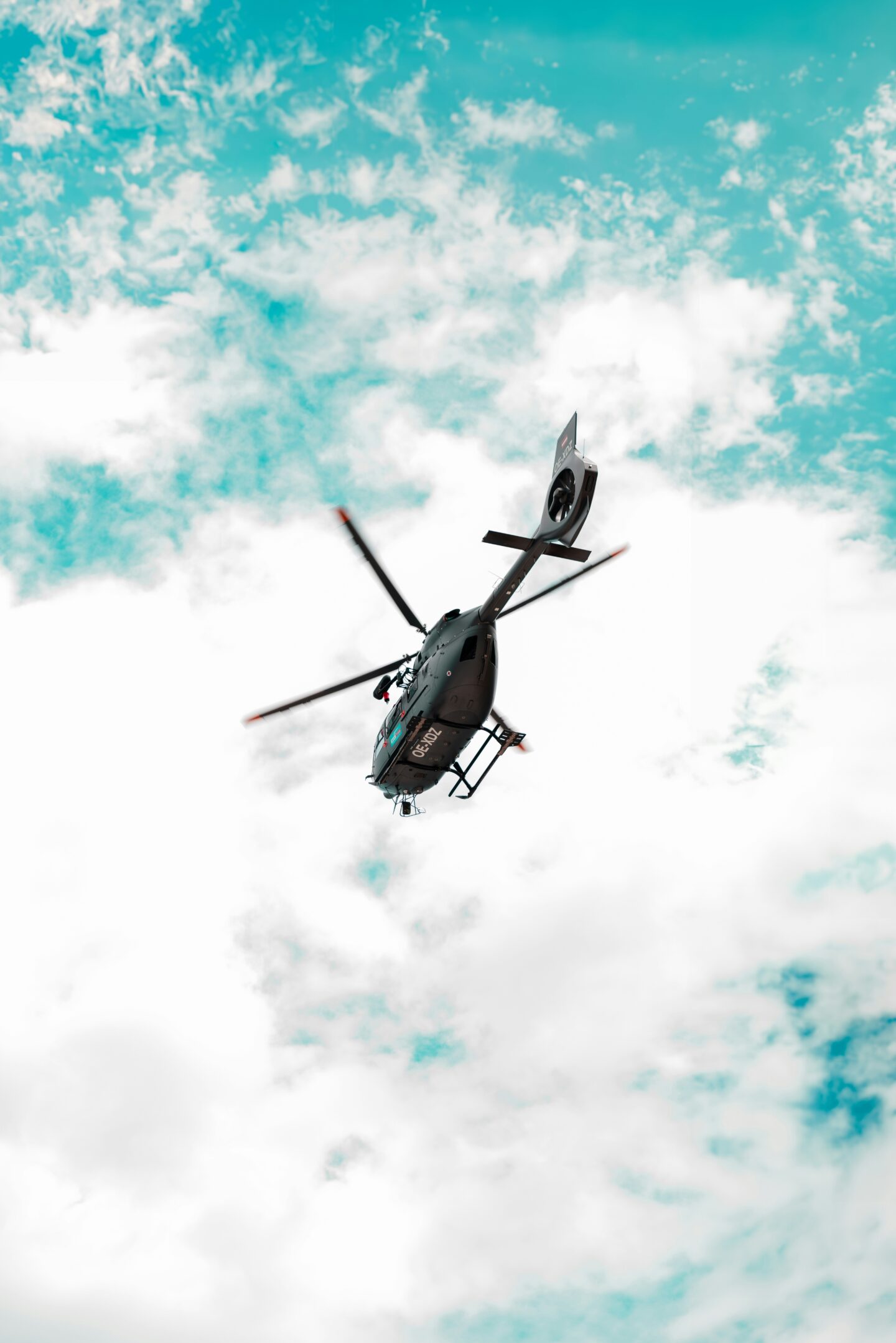 Helicopter flying through a bright blue sky with scattered clouds, viewed from below.