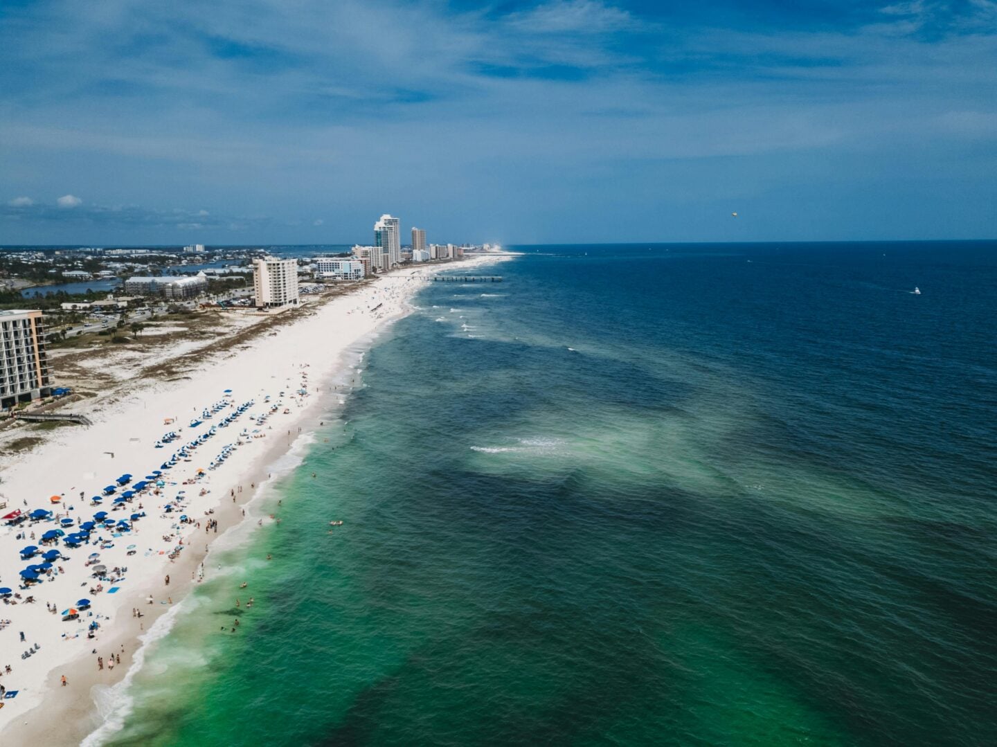 Aerial view of Gulf Shores beach in Alabama with white sand shoreline, turquoise Gulf of Mexico waters, and beachfront resorts.