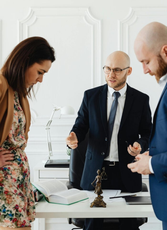 Couple standing with a divorce lawyer in an office, reviewing documents together at a desk during a legal consultation.