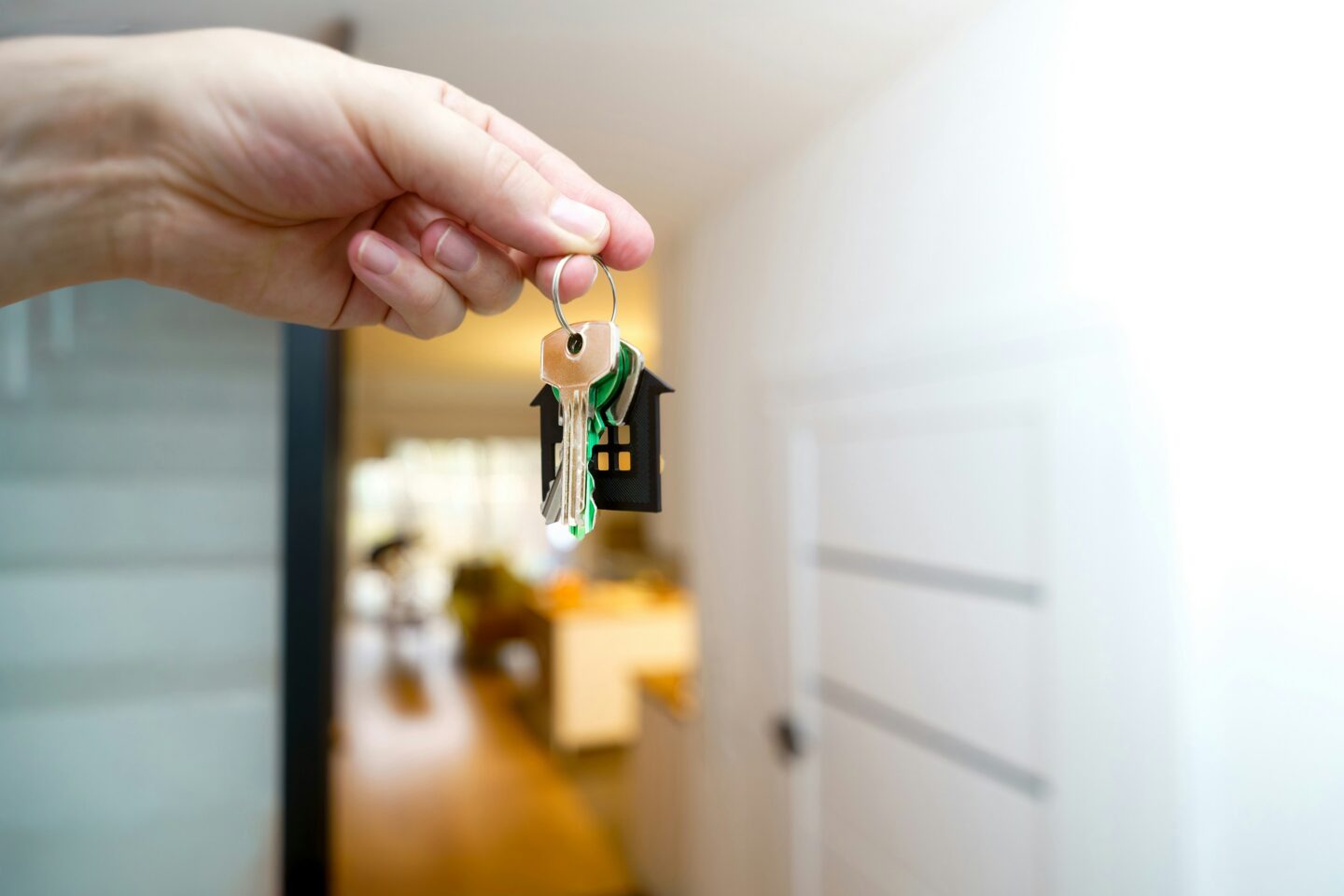 Hand holding a set of house keys with a small house-shaped keychain in front of an open doorway leading into a home interior.