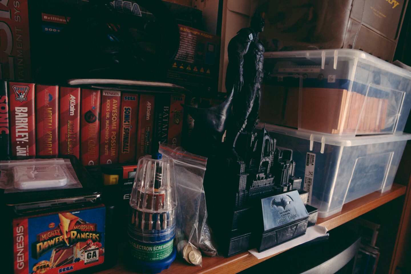 Shelves filled with retro video games, tools, and collectibles, including a Batman figurine and plastic storage bins.