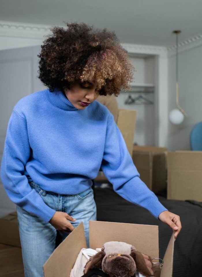 Woman packing belongings into a cardboard box during a home move, organizing personal items for a stress-free relocation.