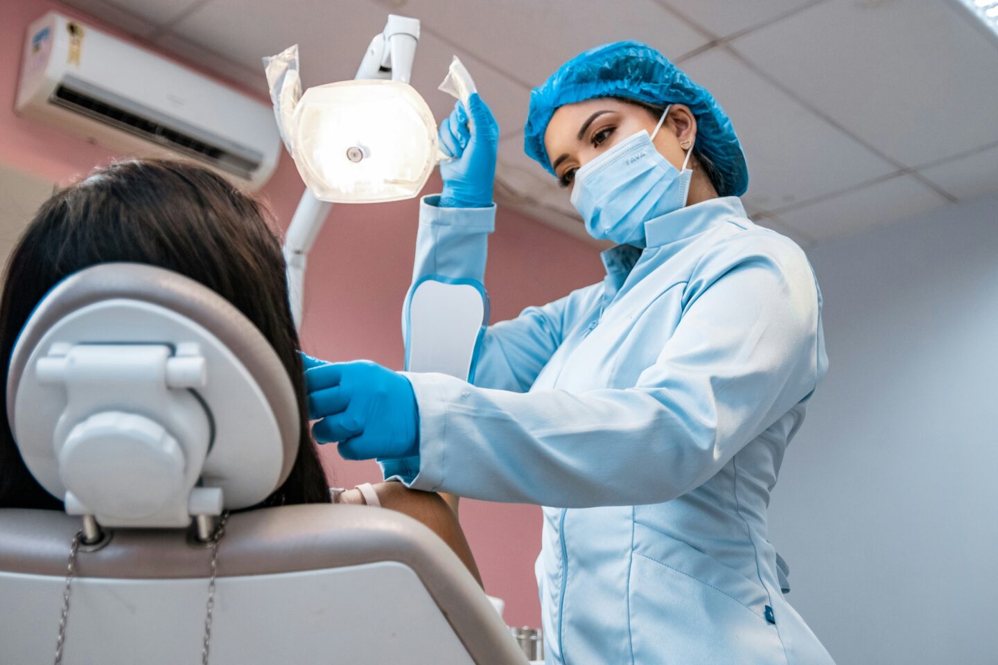Dentist wearing mask and gloves performing a preventive dental examination on a patient in a modern clinic.