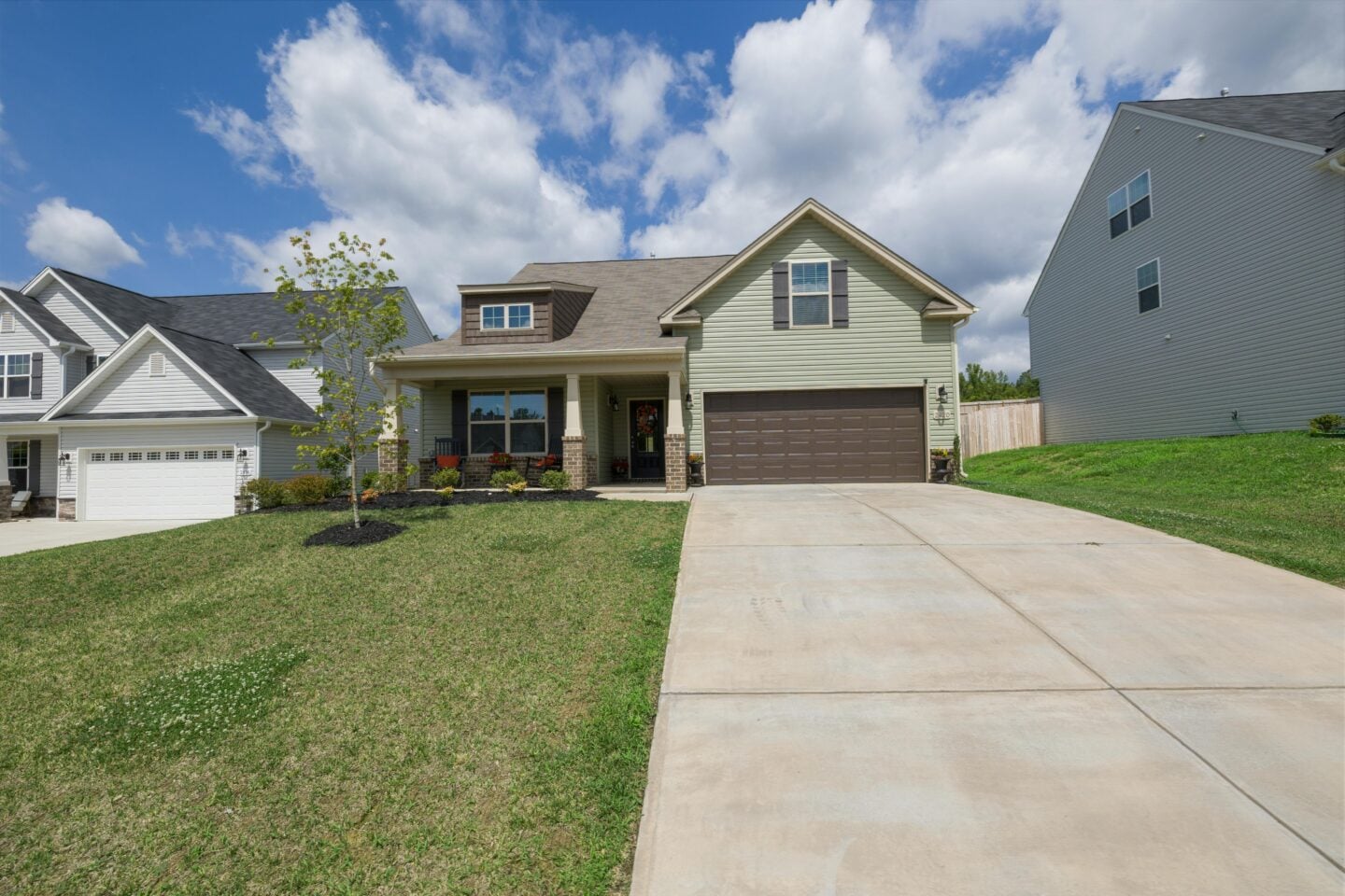 Wide view of a modern suburban home featuring a large driveway, landscaped front yard, and neighboring houses.