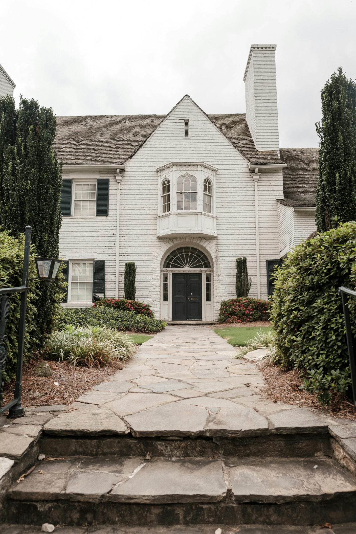 White brick house with a stone walkway leading to a black front door, framed by manicured shrubs and greenery.