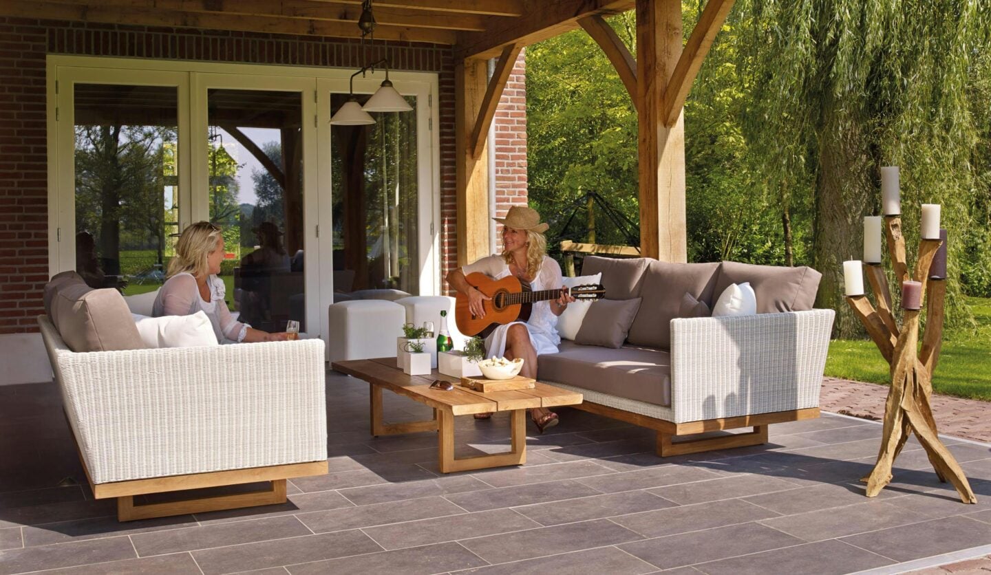 Covered outdoor patio with wicker seating, wooden beams, and stone flooring, designed for relaxing and entertaining.