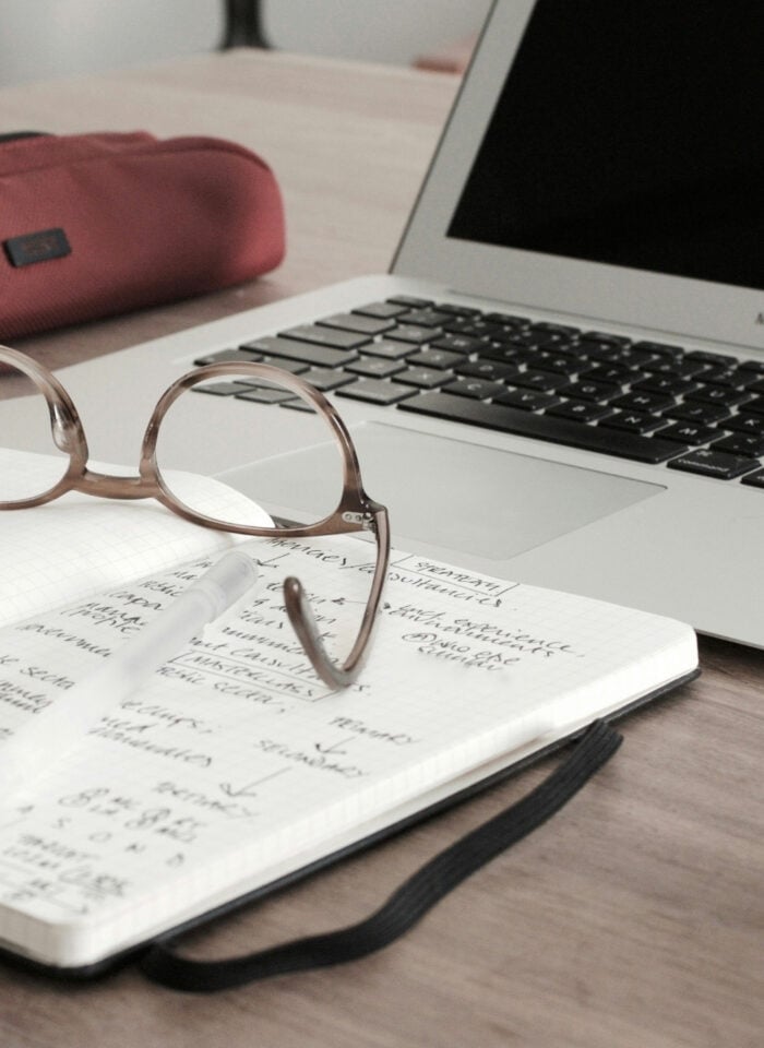 Open notebook with handwritten notes and glasses on a desk next to a laptop, representing daily life in professional school.