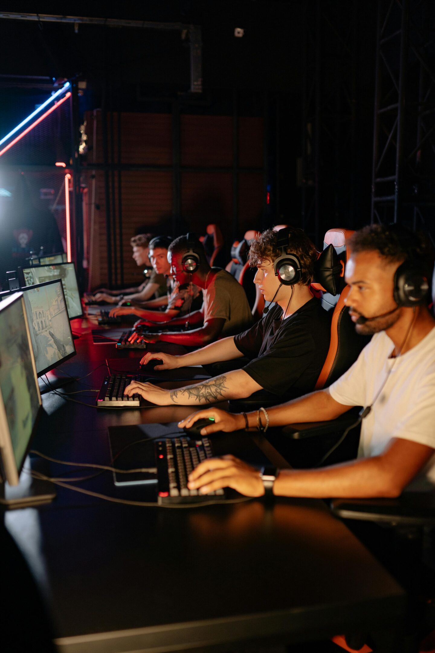 Team of esports players wearing headsets and competing at desktop gaming stations in a neon-lit tournament setup.