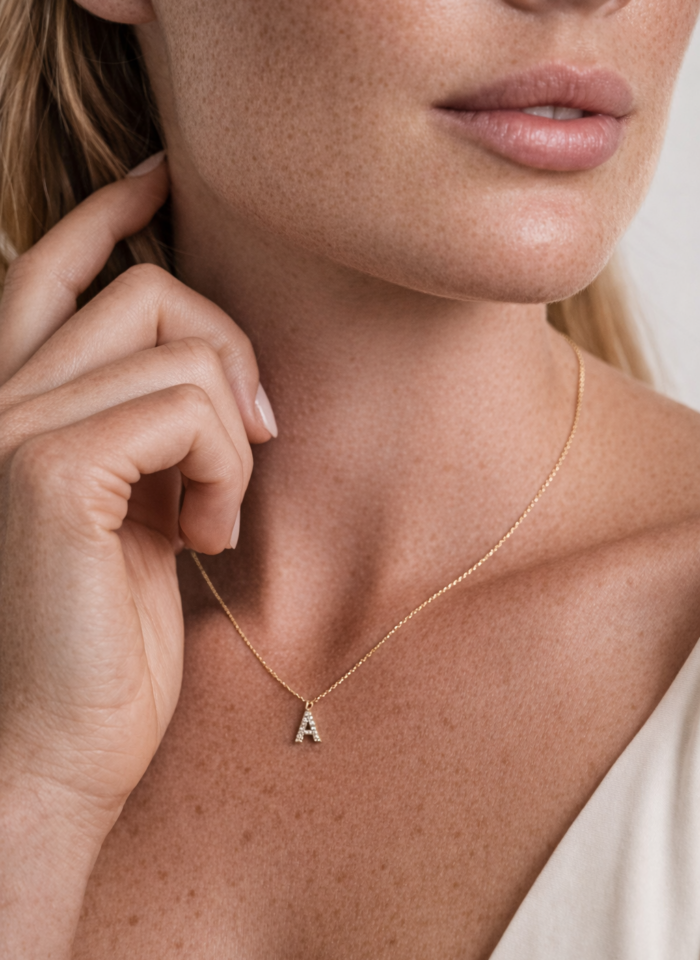 Close-up of woman wearing delicate gold initial A pendant necklace with diamond detail on fine chain.