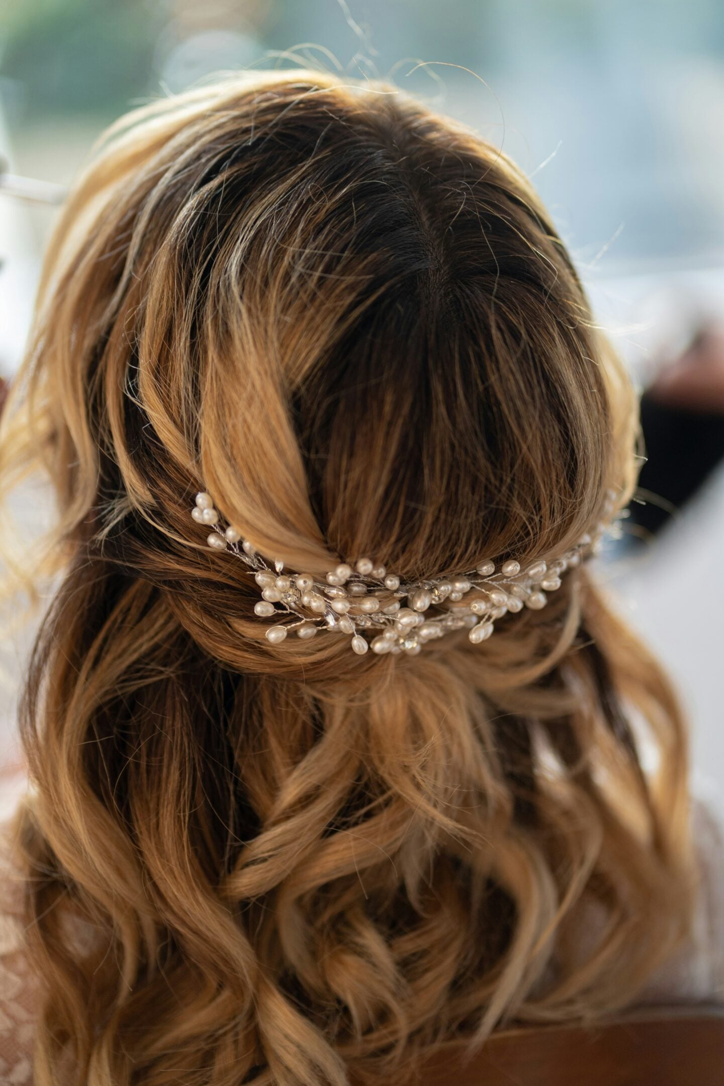 Romantic half-up prom hairstyle with loose curls and a pearl hair vine accessory, elegant formal hairstyle for prom or special occasions.