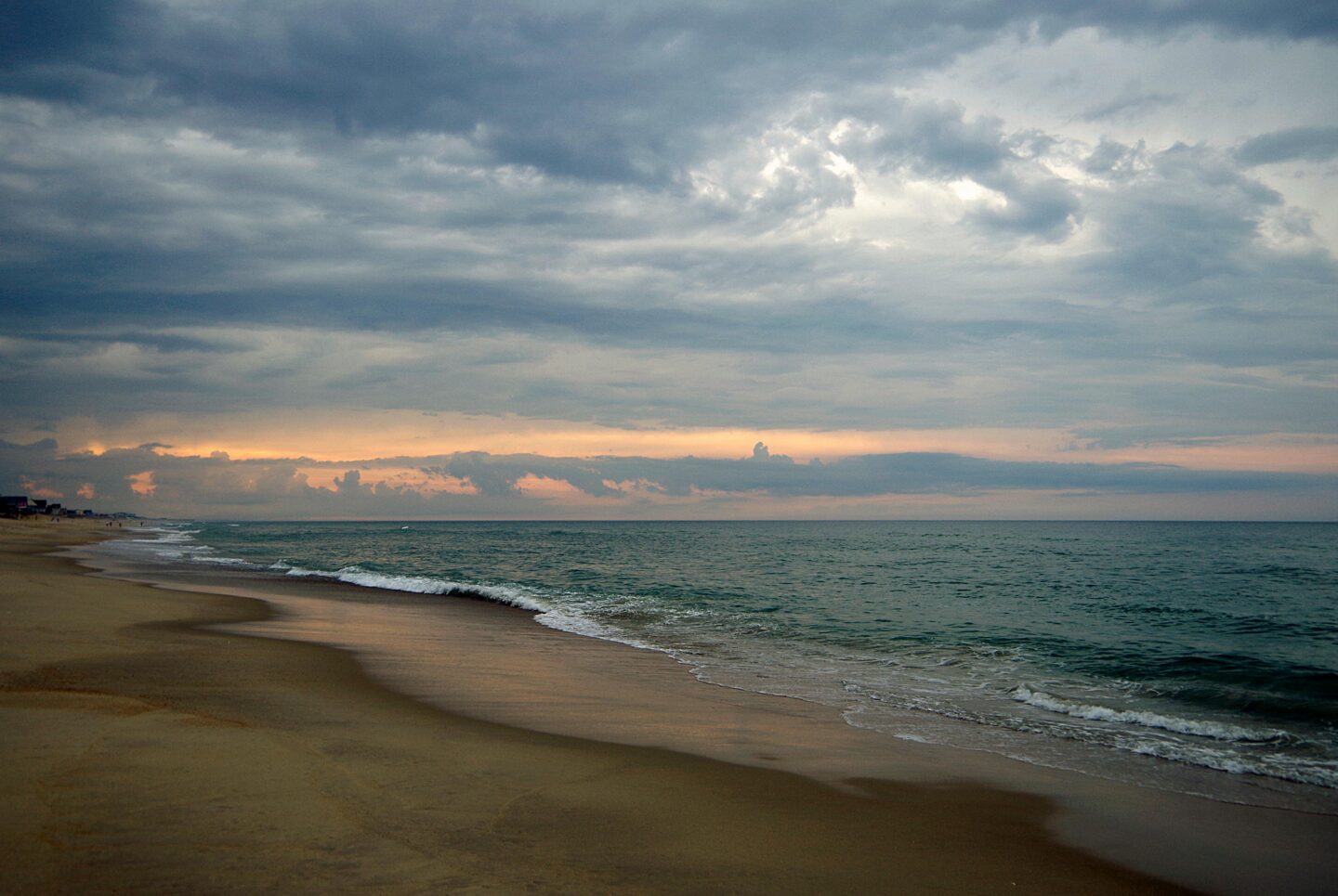 Serene sunset at Kitty Hawk beach in the Outer Banks, North Carolina, with gentle waves along sandy shoreline beneath dramatic evening clouds.