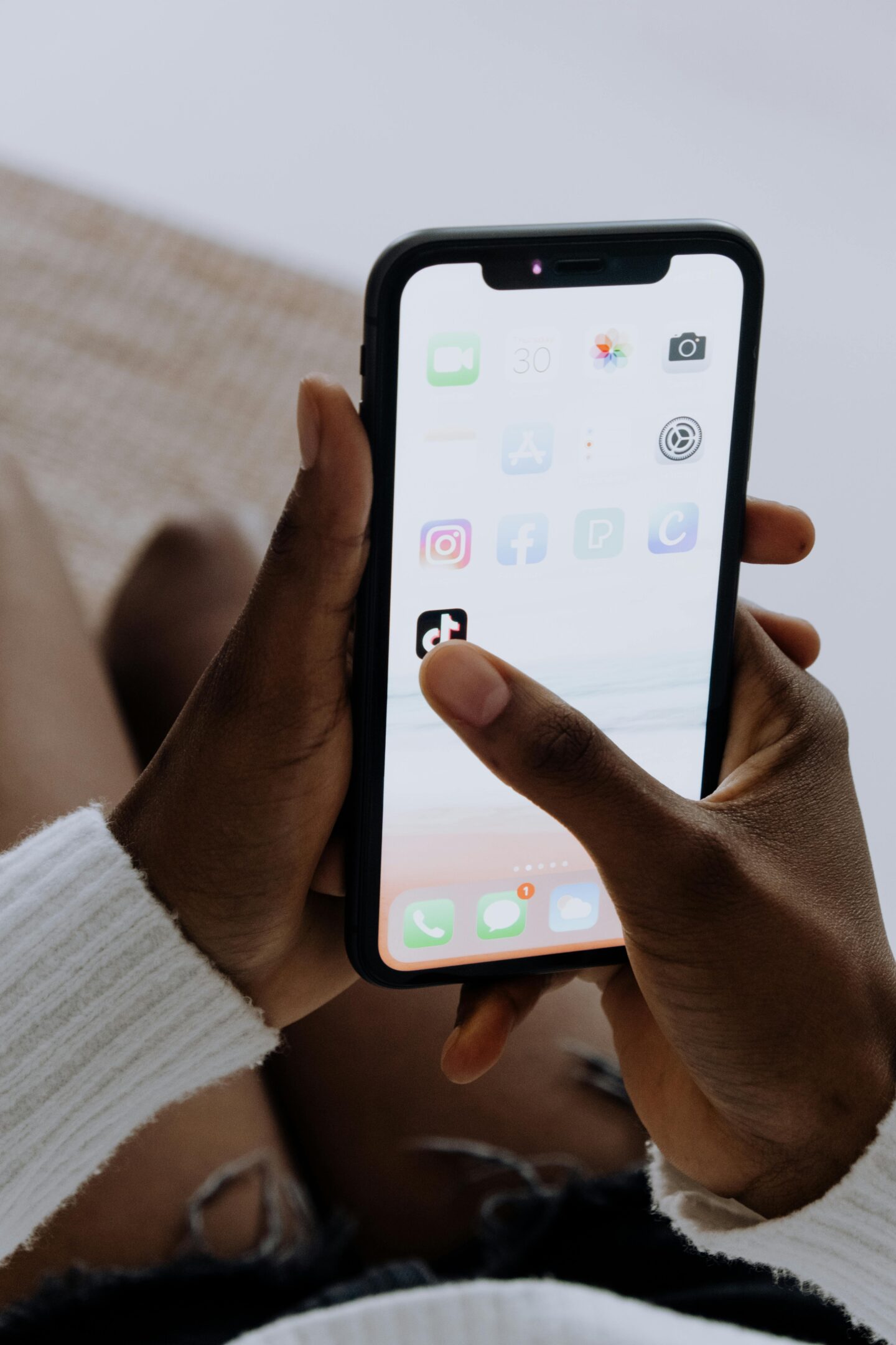 Person holding a smartphone and tapping the TikTok app icon on the home screen.