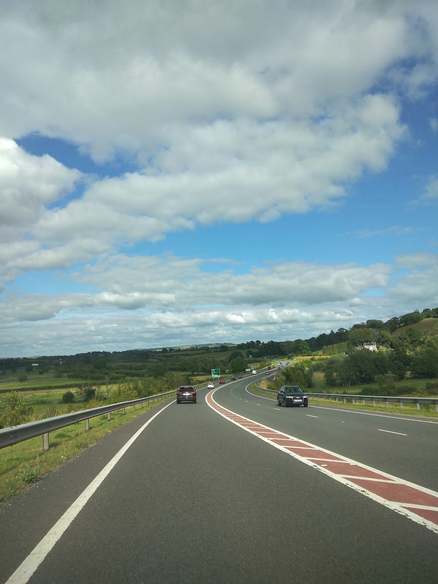 Motorway in Wales near Carmarthen with cars driving along a curved highway through green countryside under a blue sky with clouds