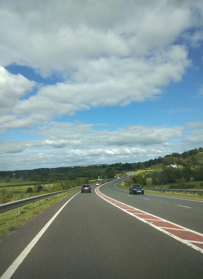 Motorway in Wales near Carmarthen with cars driving along a curved highway through green countryside under a blue sky with clouds