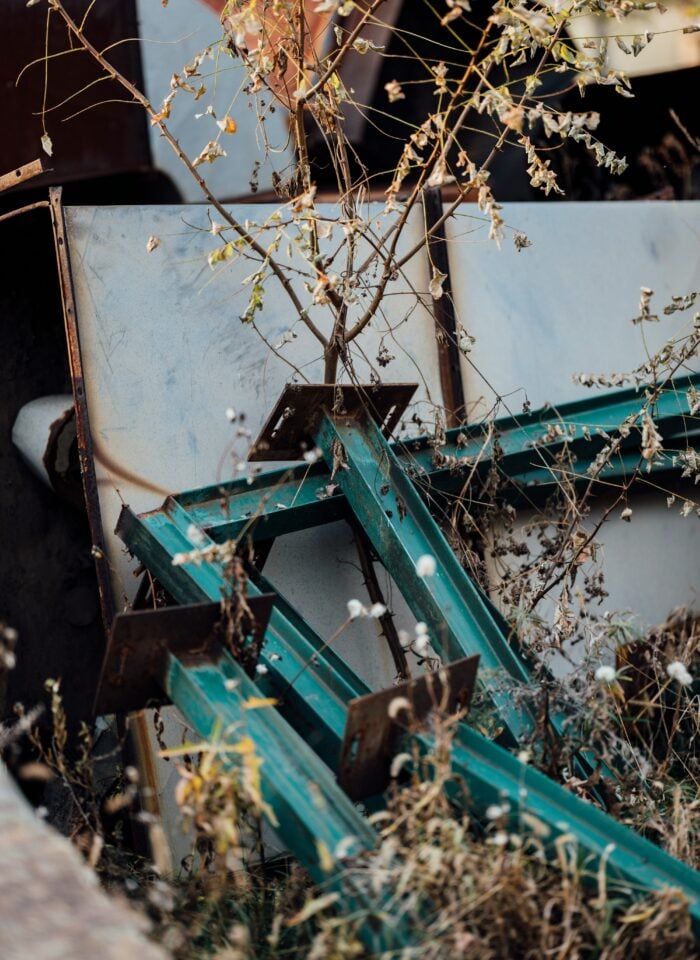 Pile of old metal beams and dried plants among backyard clutter and scrap materials ready for removal.