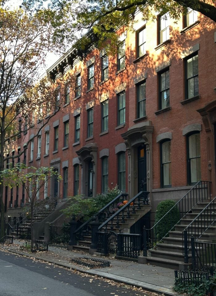 Row of classic Brooklyn brownstone houses with stoops, black railings, and autumn trees along quiet street.