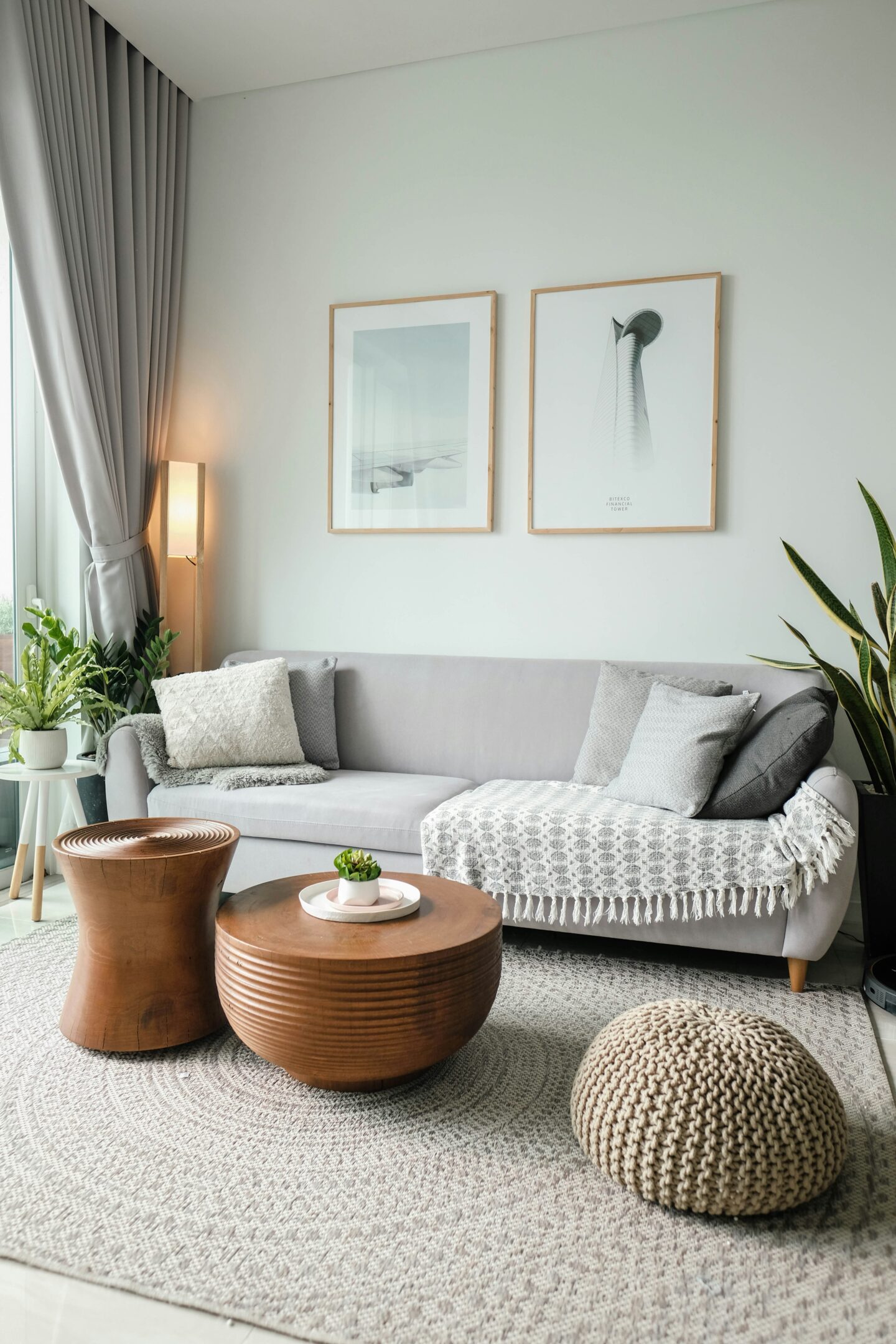 Cozy modern living room with gray sofa, wooden coffee tables, textured rug, plants, and framed wall art in neutral tones