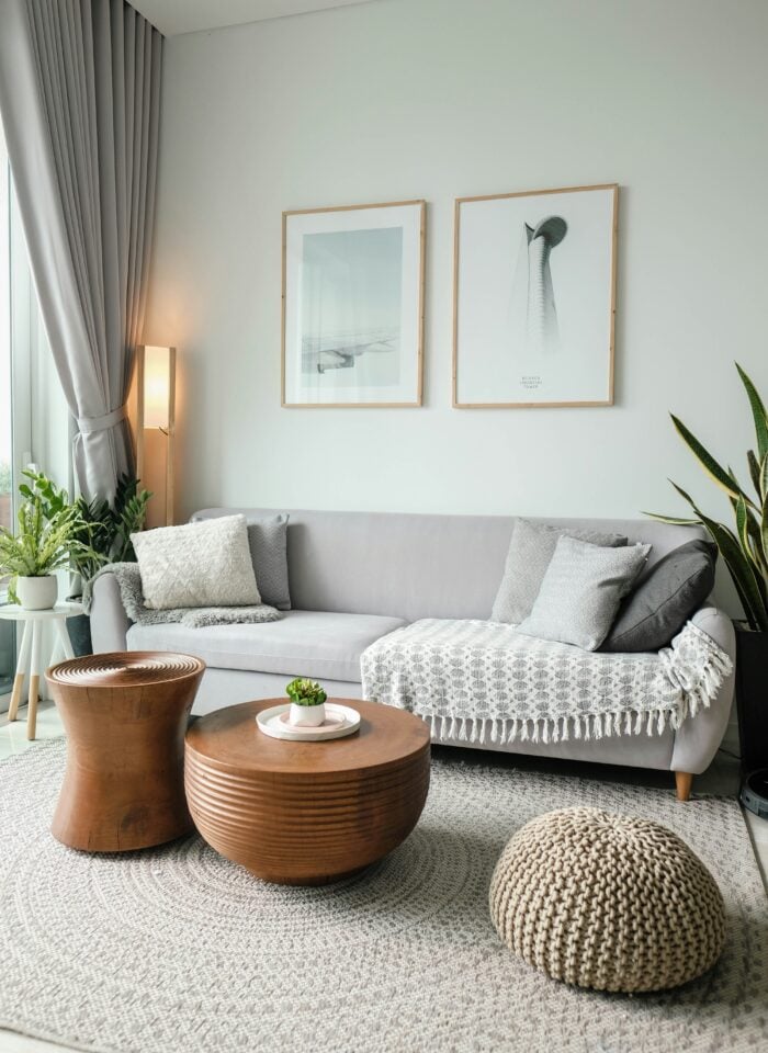 Cozy modern living room with gray sofa, wooden coffee tables, textured rug, plants, and framed wall art in neutral tones