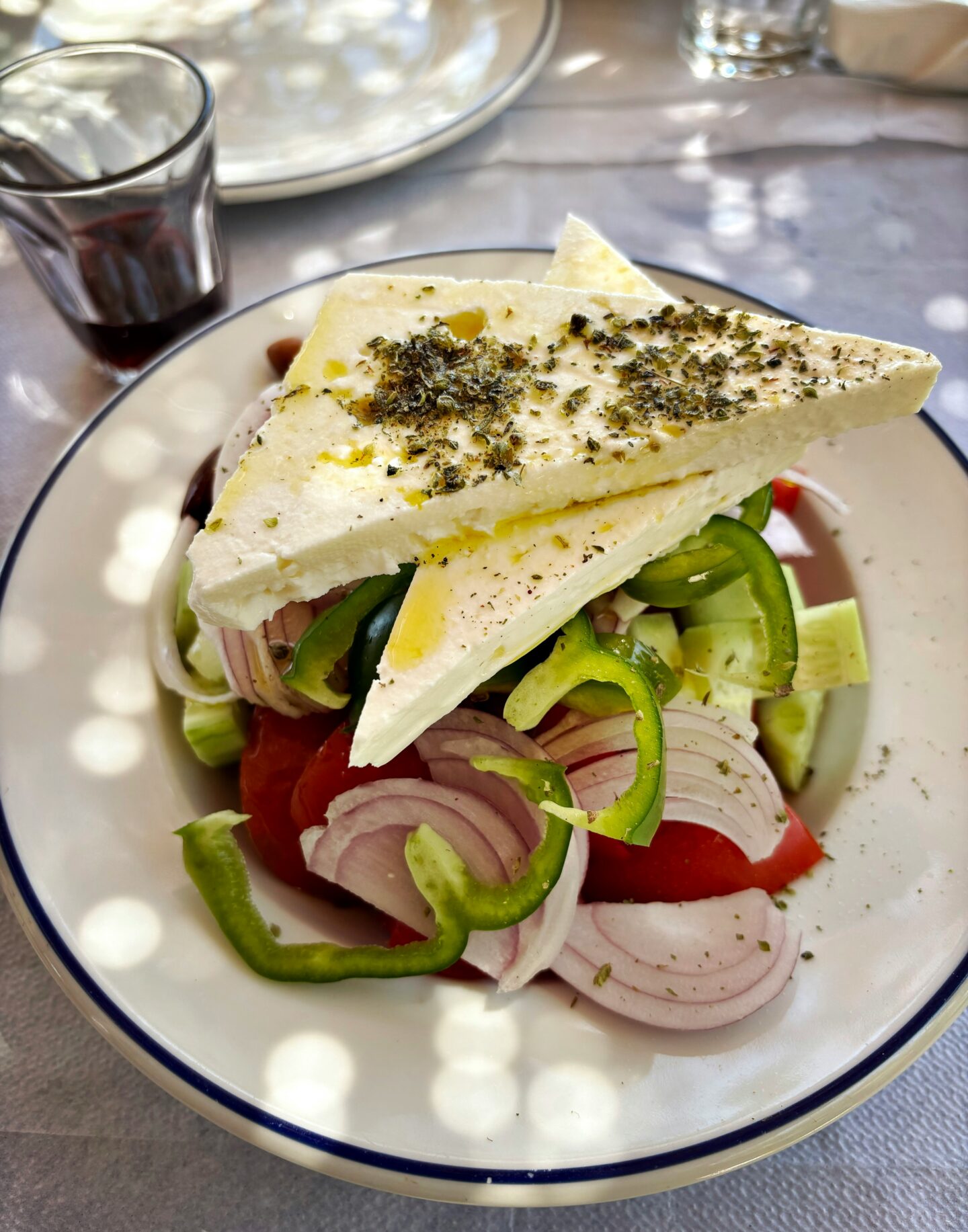 Greek salad with large slices of feta cheese, tomatoes, cucumber, green peppers, and red onion drizzled with olive oil.