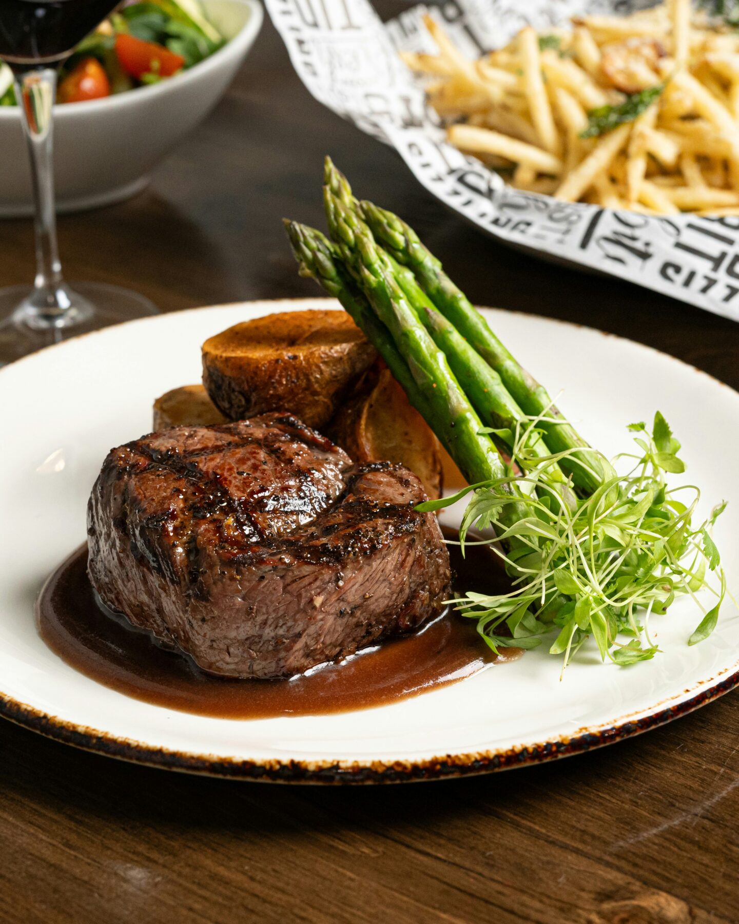 Grilled steak served with asparagus, roasted mushroom, microgreens, and rich sauce on a white plate.