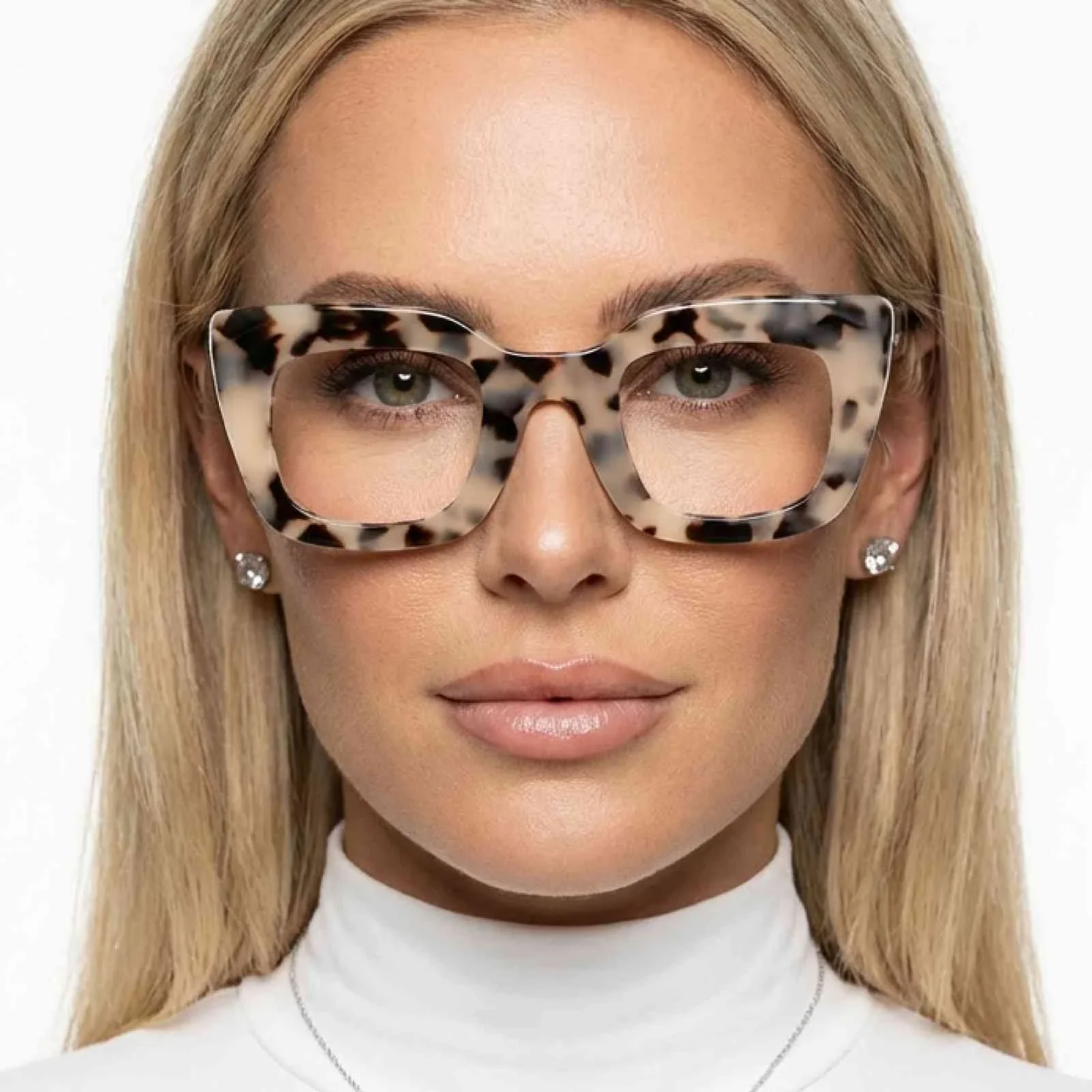 Close-up portrait of woman wearing oversized tortoiseshell eyeglasses, blonde hair and neutral makeup, stylish accessories with minimal white background.