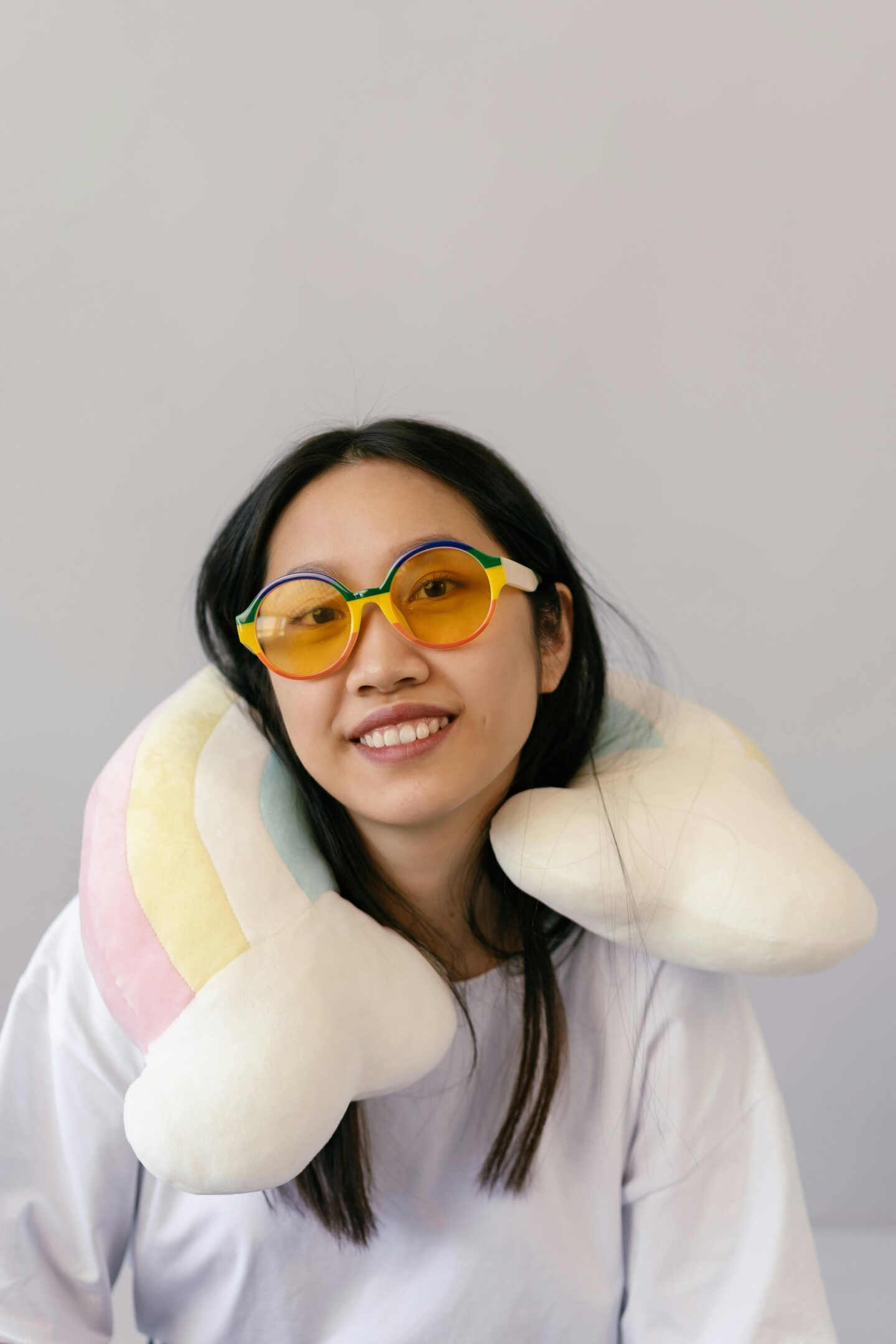 Smiling traveler wearing colorful sunglasses and a soft travel neck pillow for comfort on long journeys.