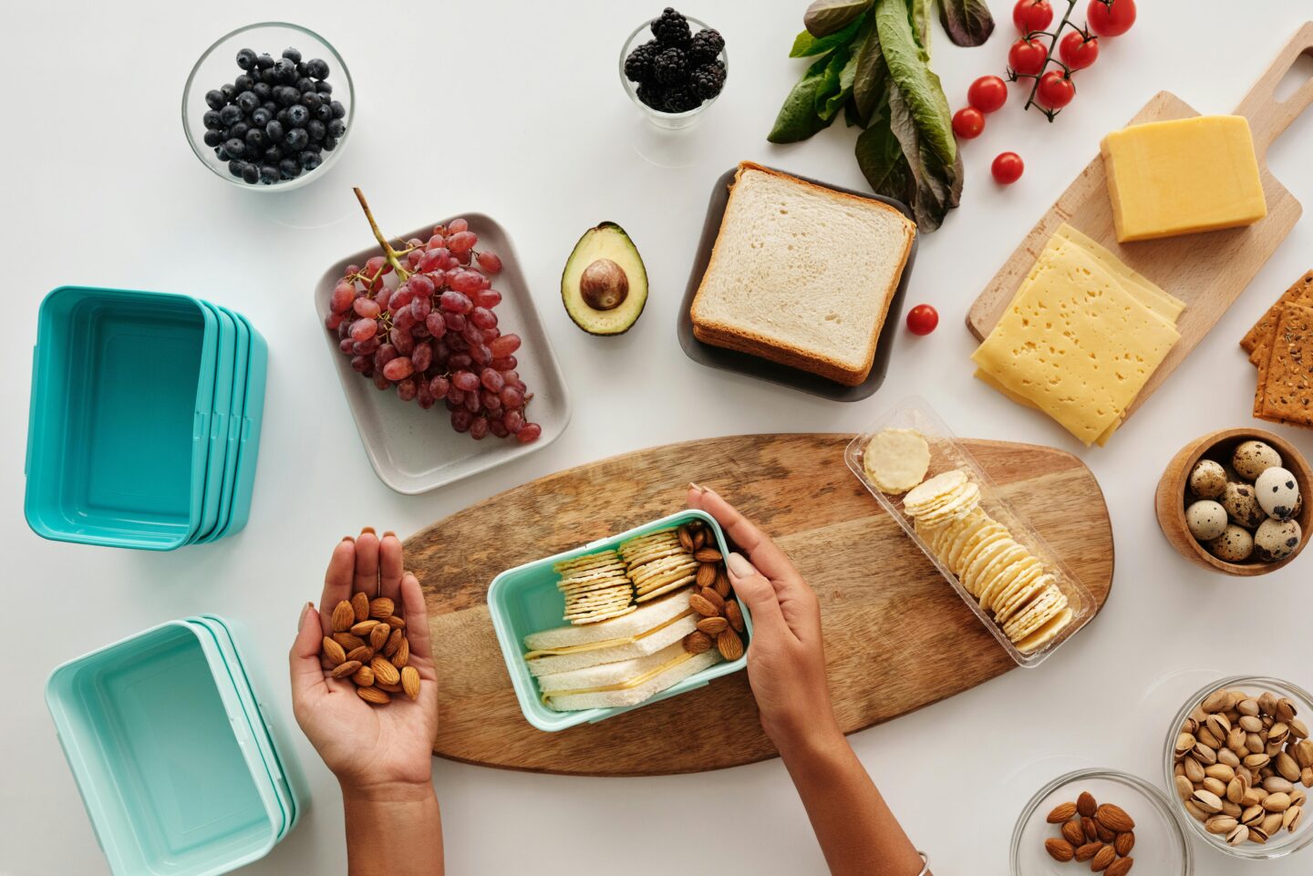 Preparing healthy travel snacks with almonds, crackers, fruit, bread, and cheese in reusable containers.