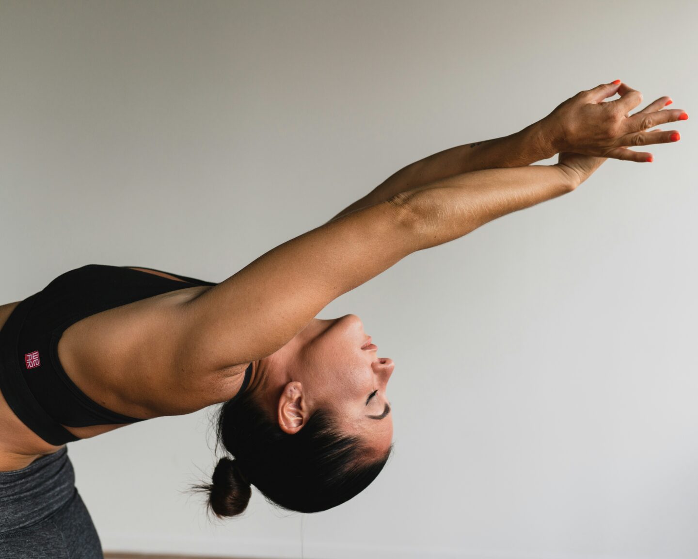 Woman stretching her arms during a yoga or morning exercise routine against a neutral background.