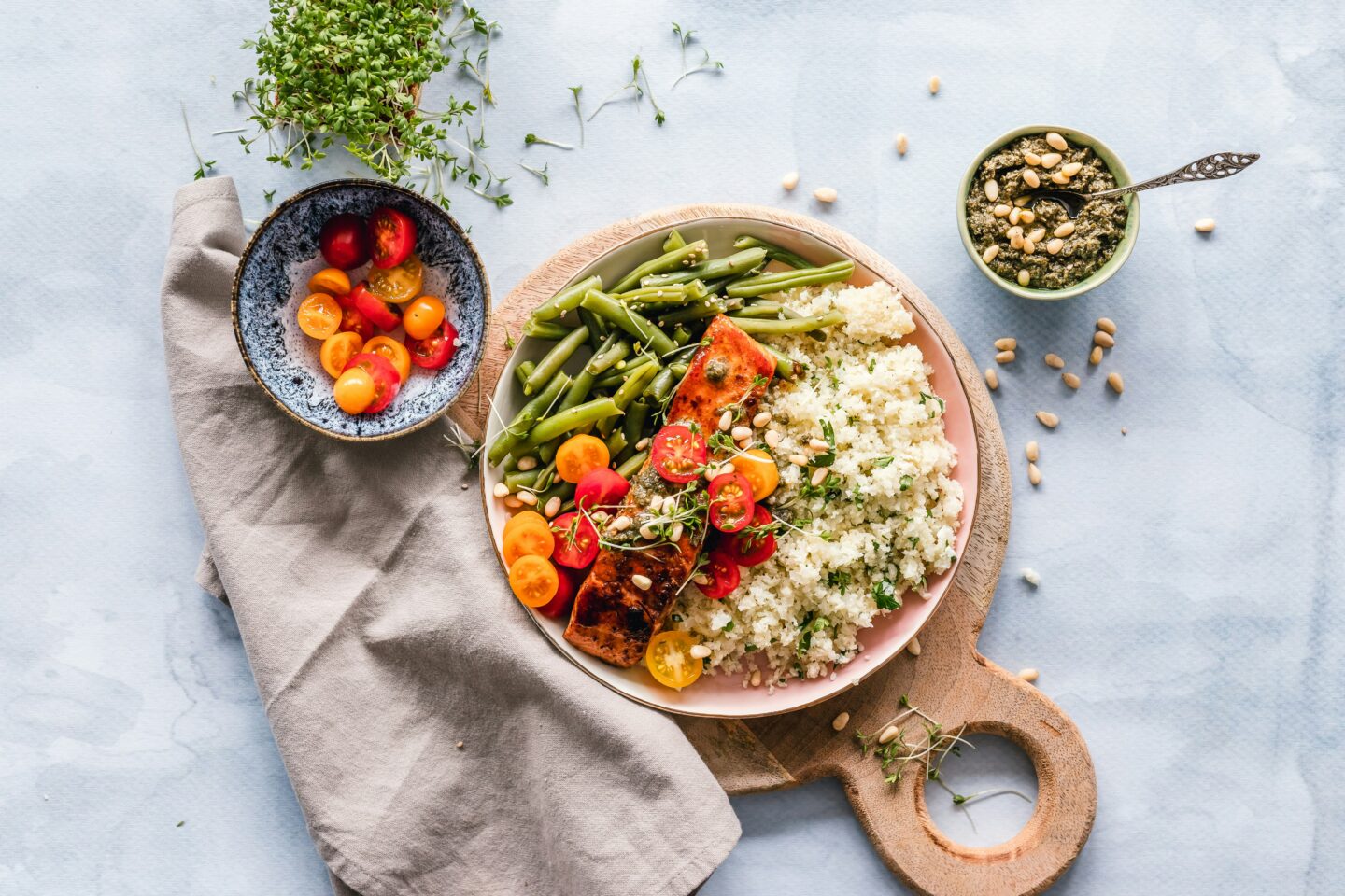 Healthy meal with grilled salmon, green beans, couscous, and cherry tomatoes served on a wooden board.