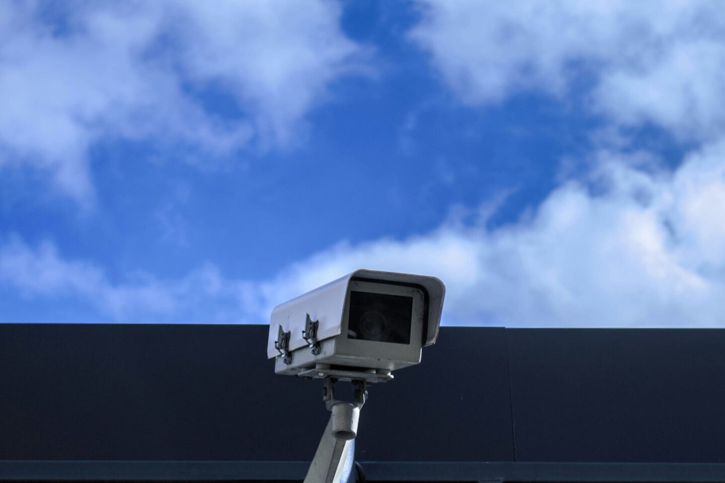 Outdoor CCTV security camera mounted on a building monitoring property against a blue sky background.