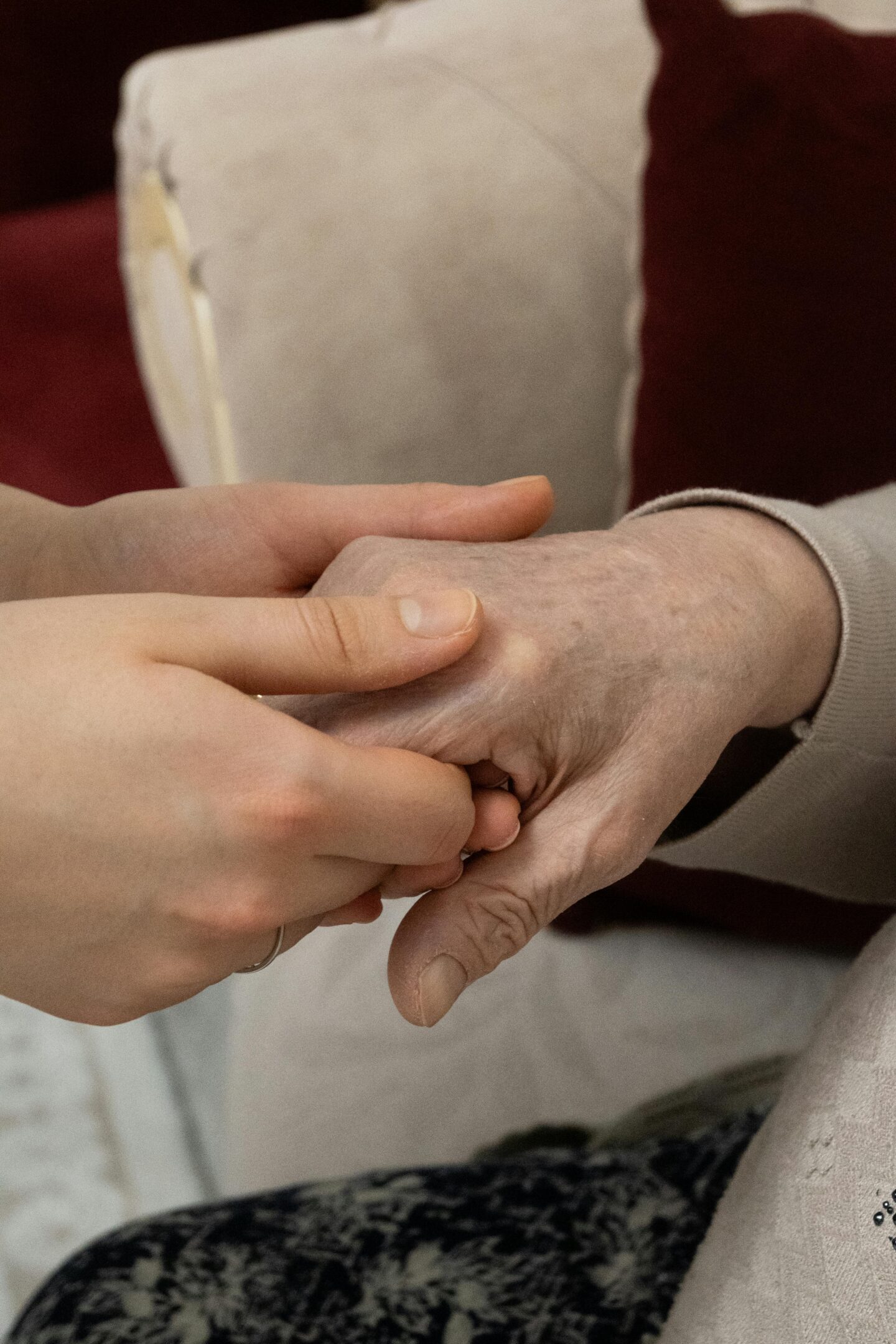 Close-up of a caregiver gently holding and supporting an elderly person’s hand, showing care and assistance in an indoor setting.