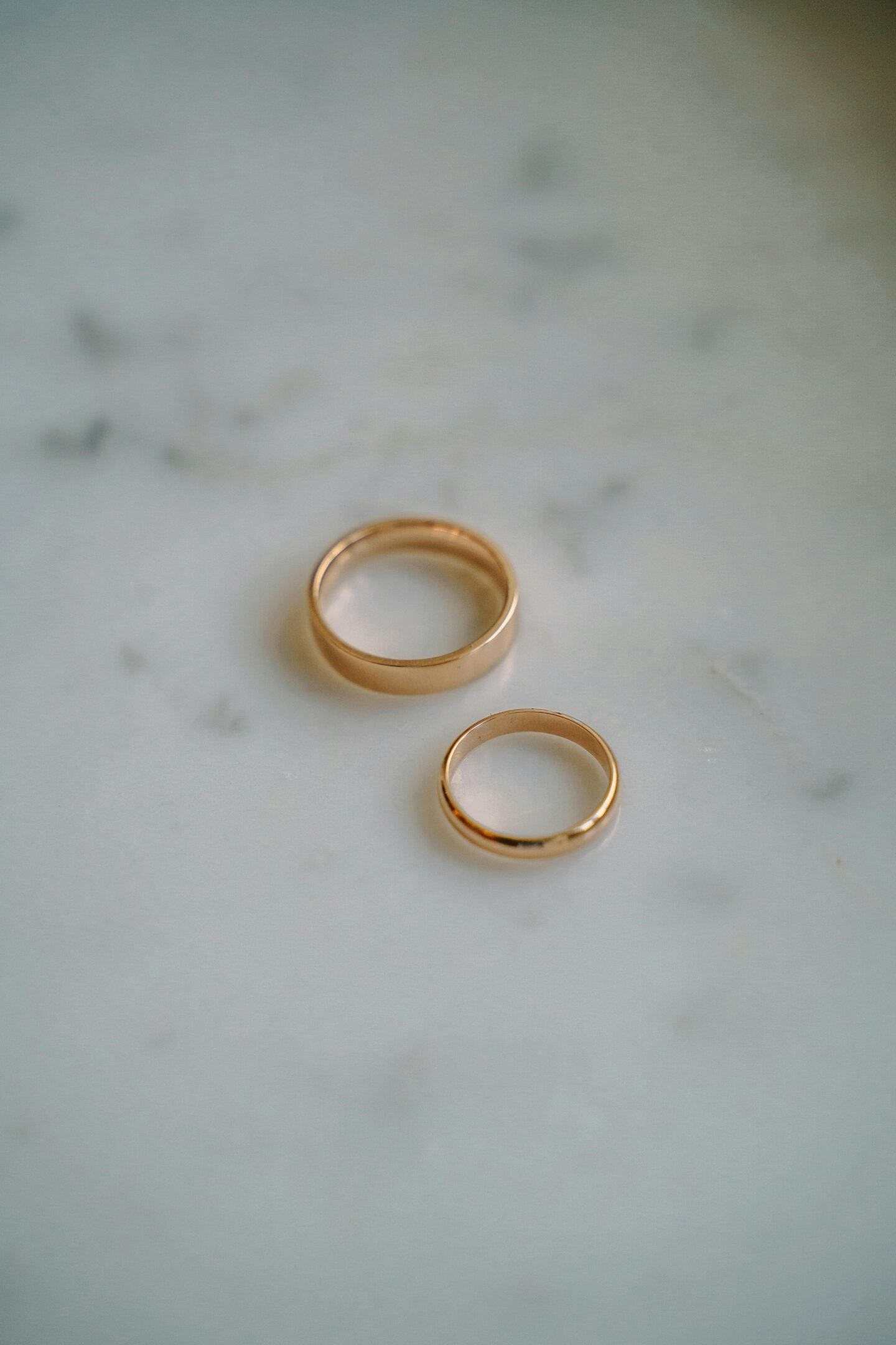 Gold wedding bands placed on a light marble surface, minimal and elegant ring set for couples, soft natural lighting, close-up detail of polished gold ring. 