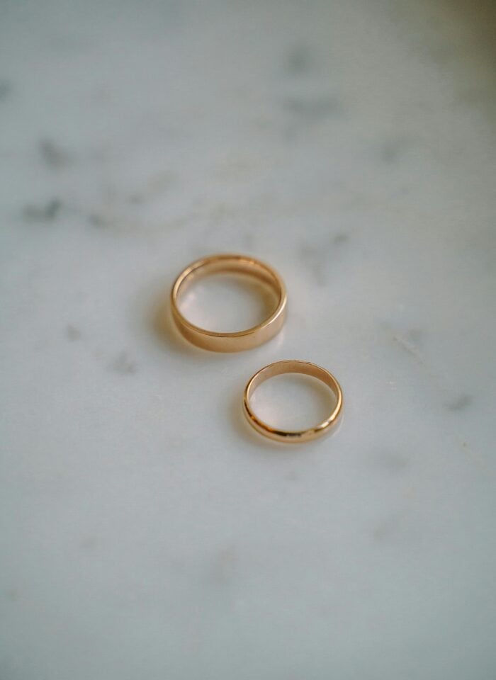 Gold wedding bands placed on a light marble surface, minimal and elegant ring set for couples, soft natural lighting, close-up detail of polished gold ring.