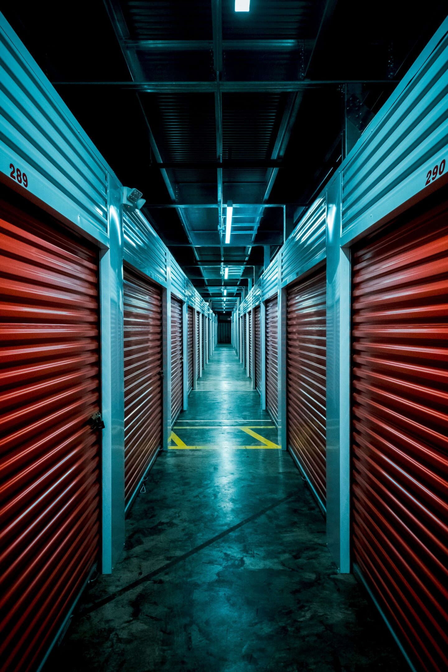 Long corridor of self storage units with red roll-up doors and bright overhead lighting in modern facility