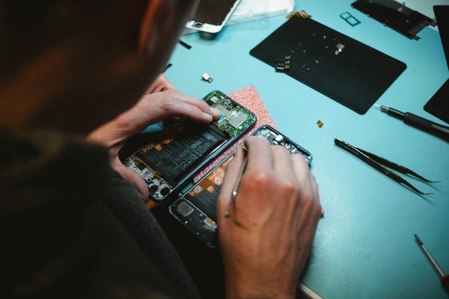 Technician repairing a smartphone with internal components exposed on a repair workbench.