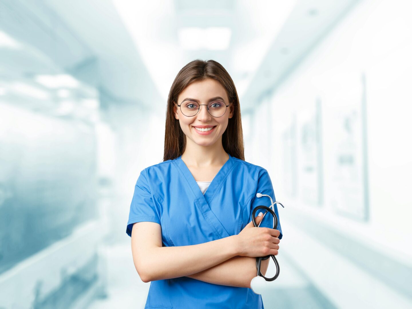 Smiling female nurse in blue scrubs holding a stethoscope, standing in a bright hospital corridor with a clean clinical background.