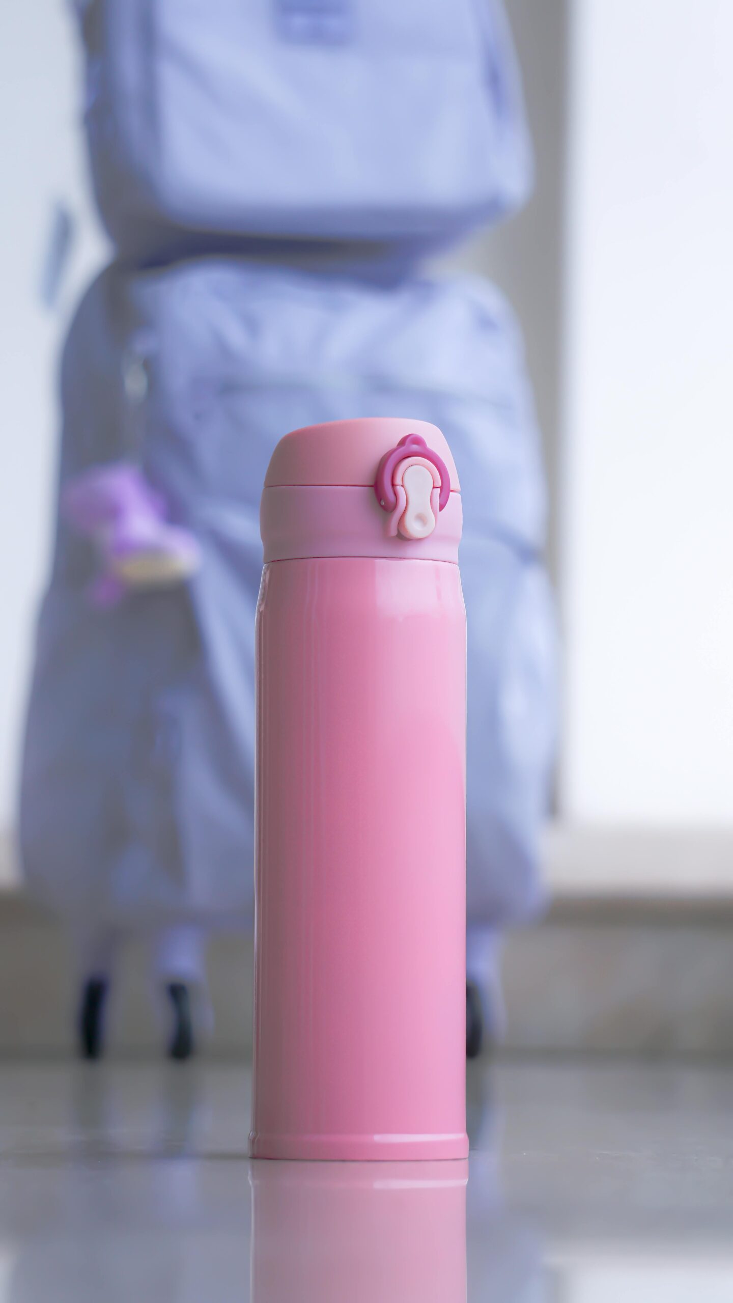 Pink insulated travel tumbler standing on the floor in front of a light blue suitcase, ready for a trip.