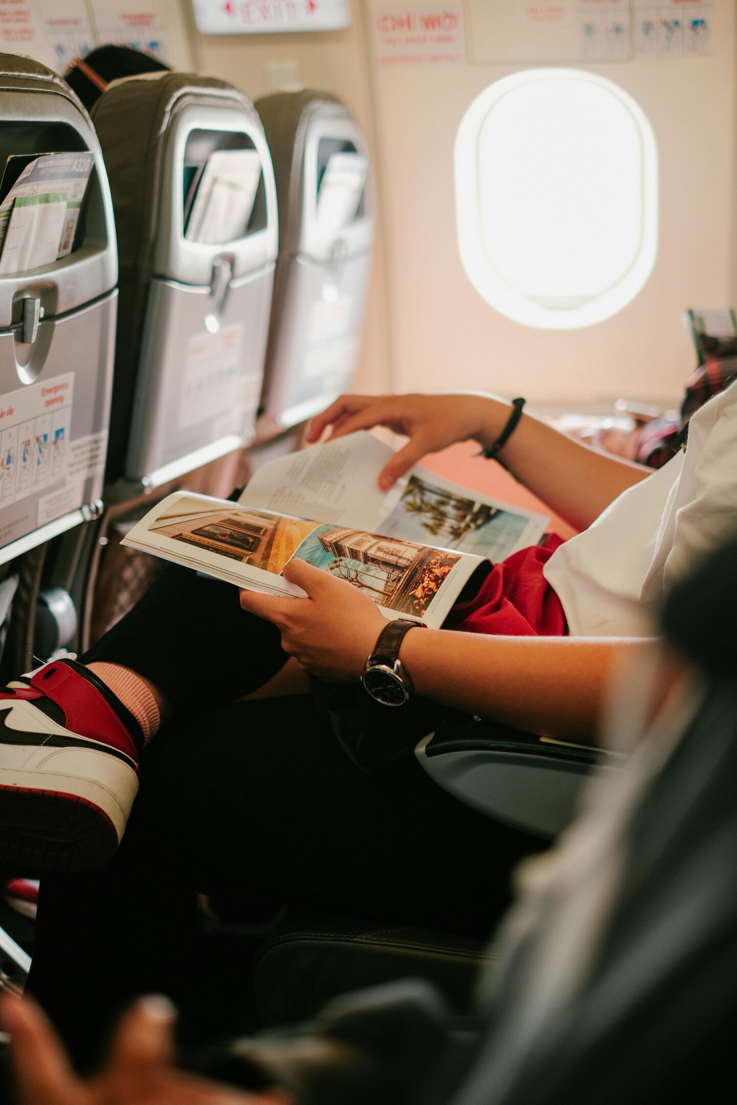 Passenger reading a travel magazine while sitting in an airplane seat during a flight.