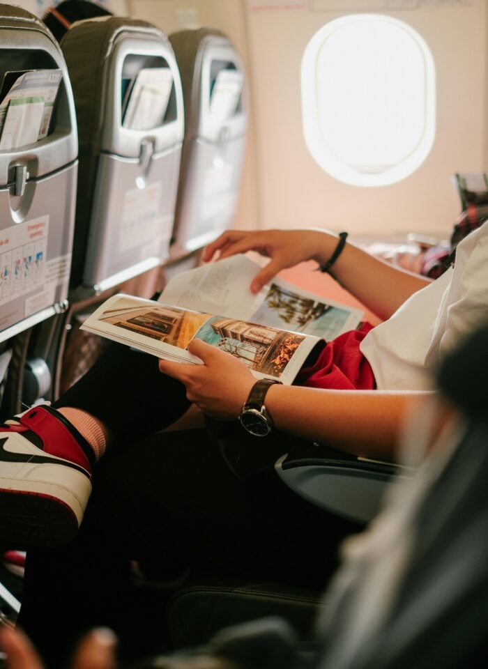 Passenger reading a travel magazine while sitting in an airplane seat during a flight.