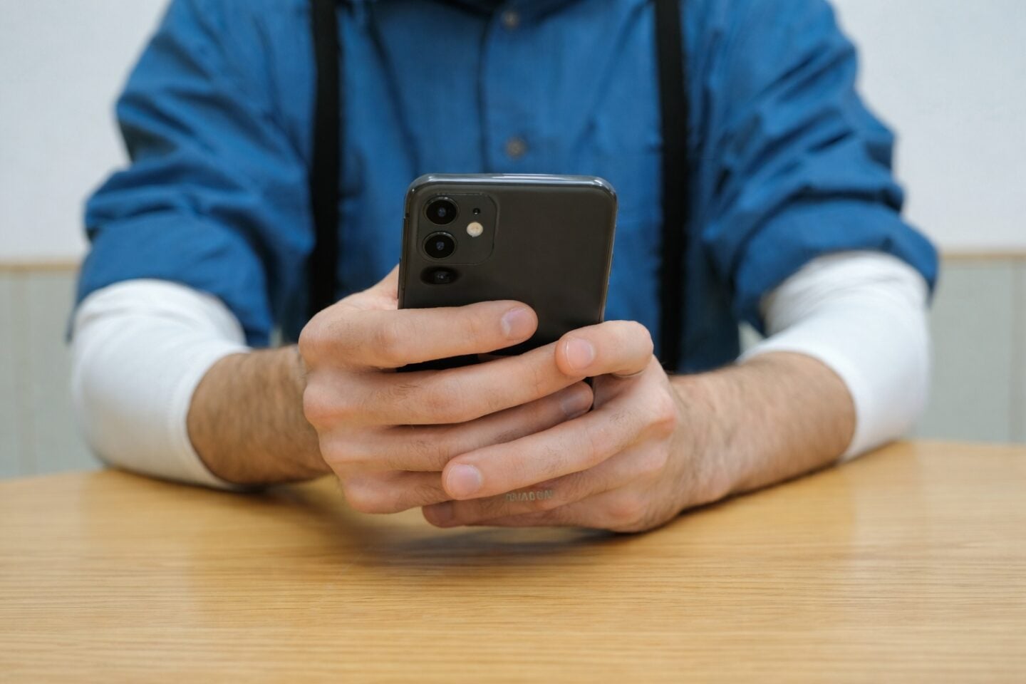 Person holding a modern smartphone with triple camera setup while sitting at a wooden table.