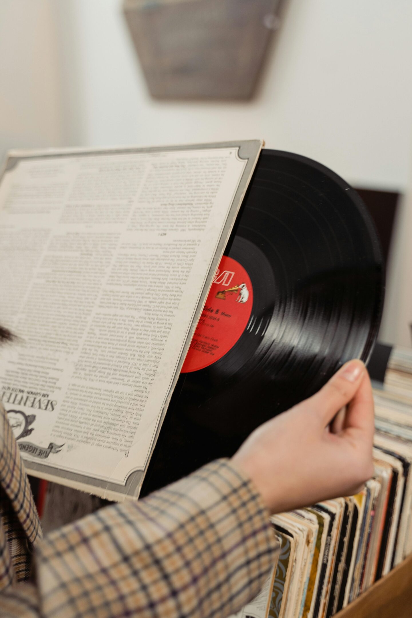 Person holding a vinyl record partially out of its sleeve above a crate of records, showcasing a classic collection of vintage albums.