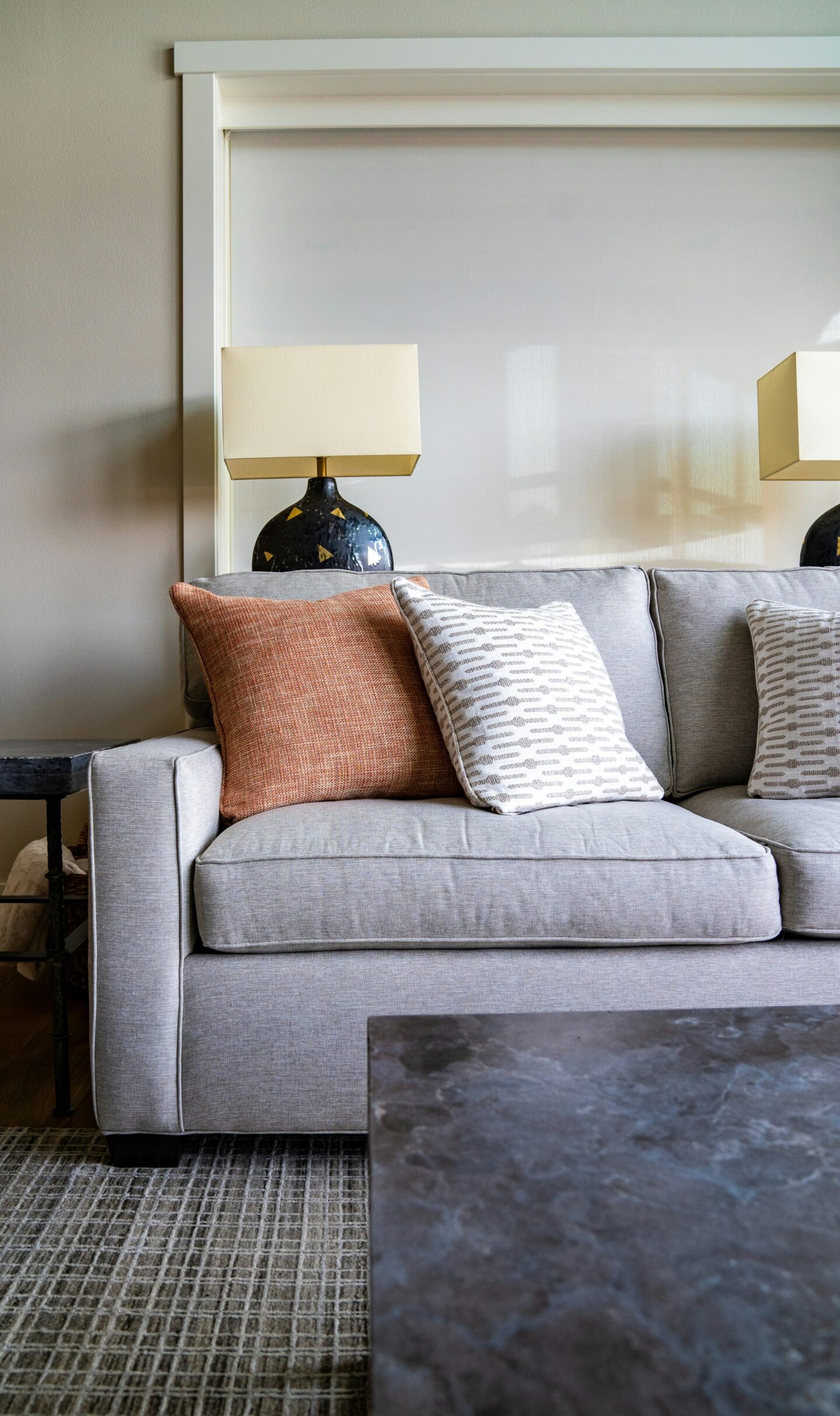 Modern living room with grey fabric sofa, decorative throw pillows, table lamps and neutral decor, cozy minimalist interior design with soft textures and warm lighting.